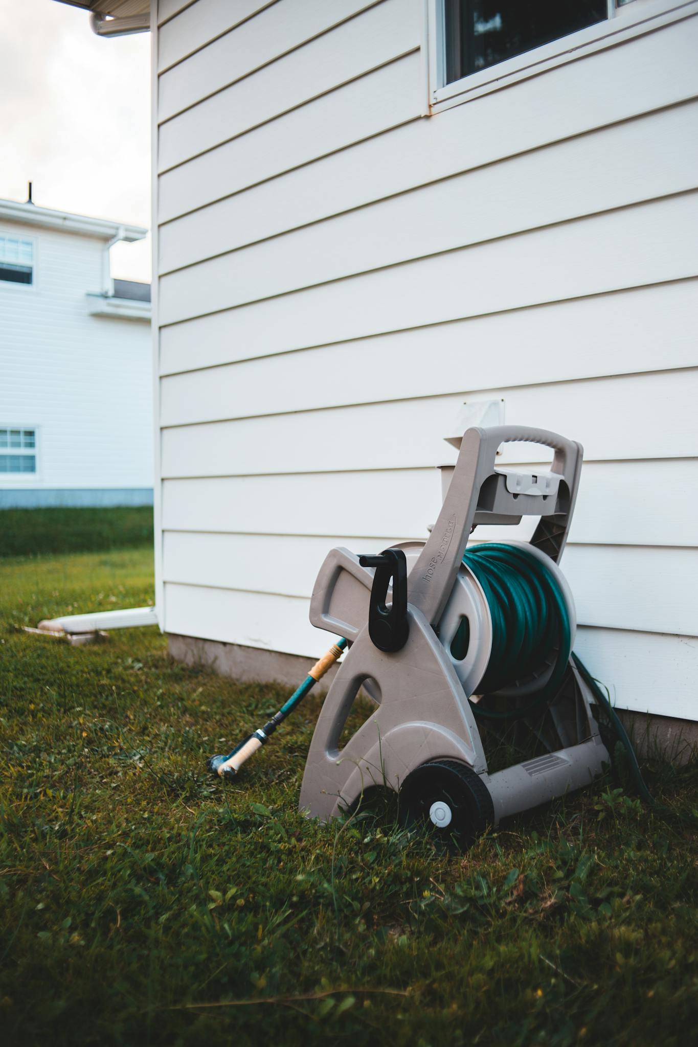 Close-up of a rolled water hose on a reel next to a house wall.