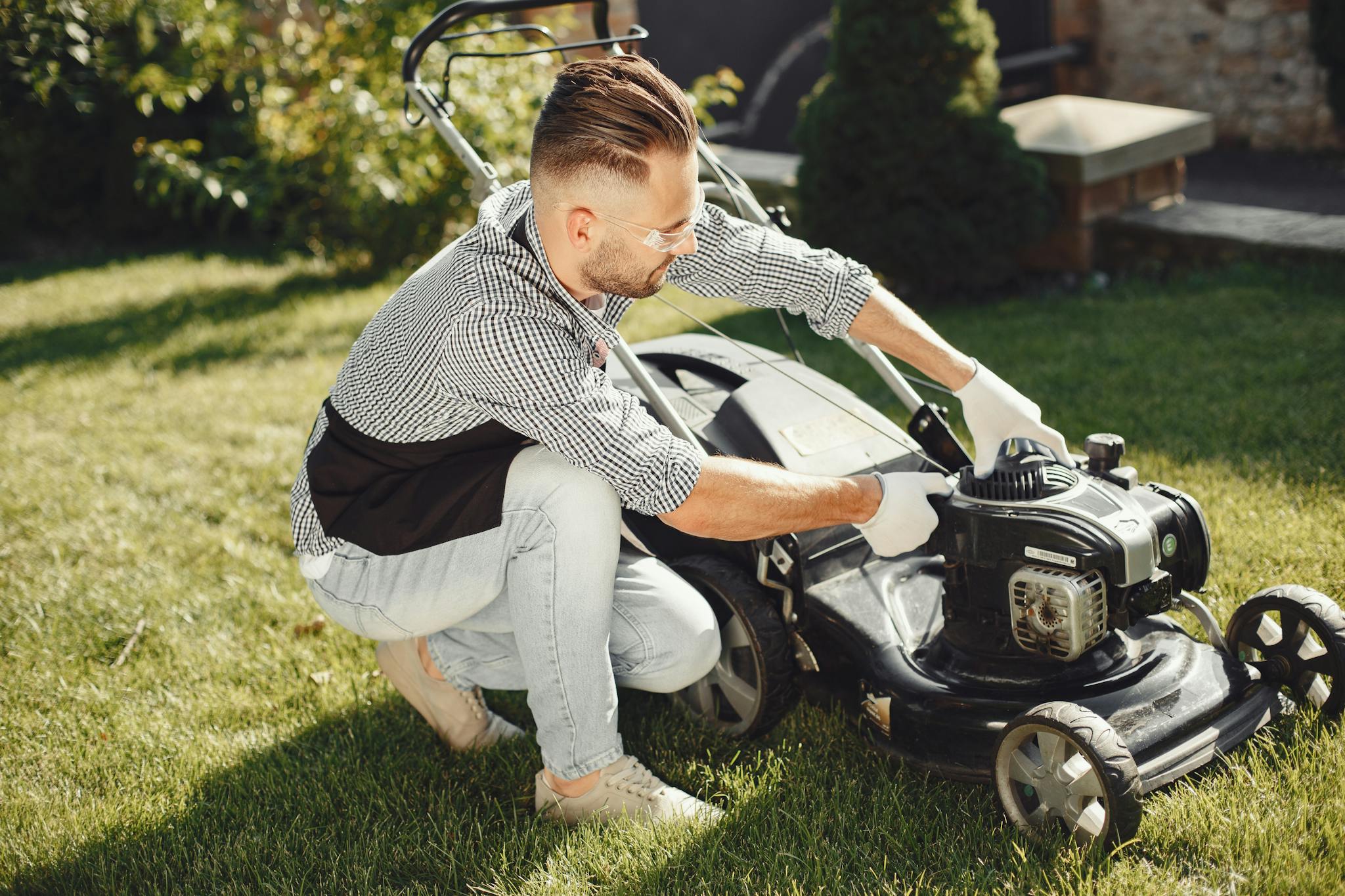 Man preparing lawn mower for garden work on a sunny day outdoors.